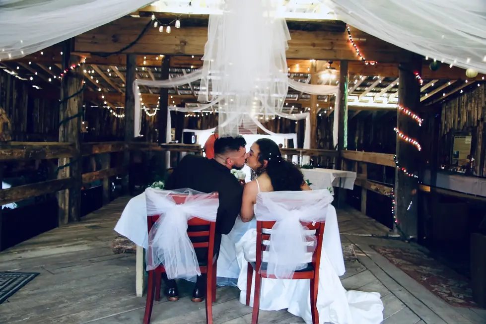 A couple kissing at their sweetheart table inside the decorated barn