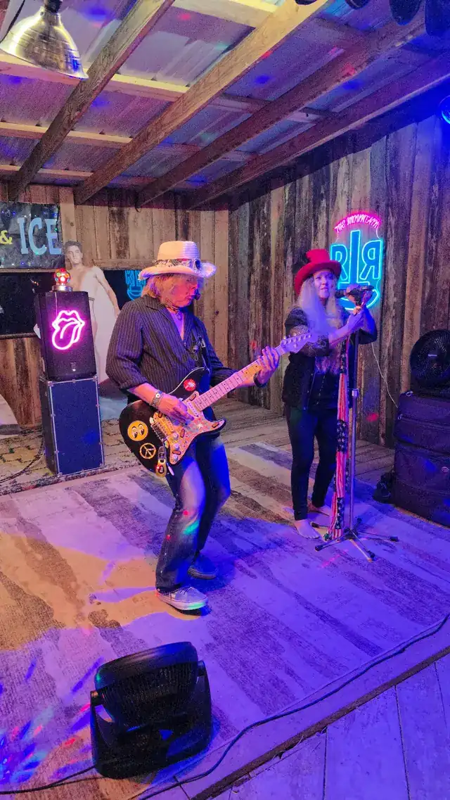 Two musicians performing beside the glowing RTR neon sign on the barn stage